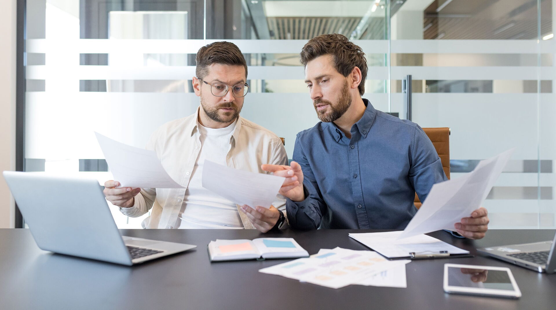 Two men are sitting in a conference room, reviewing documents.