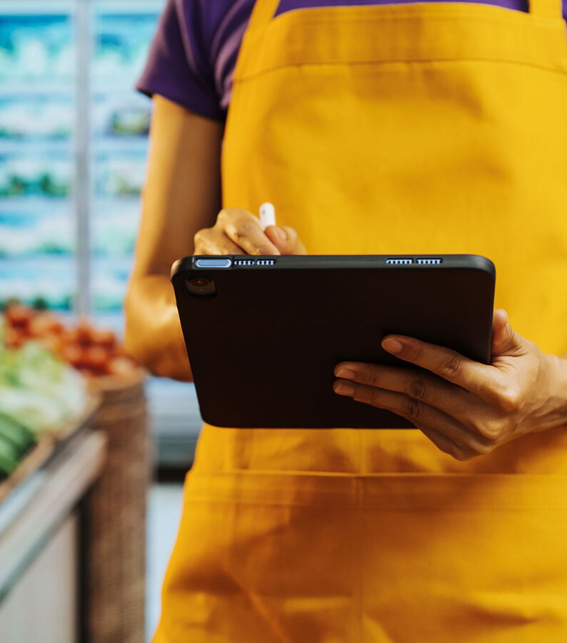 Eine Mitarbeiterin eines Supermarktes prüft Daten auf einem Tablet