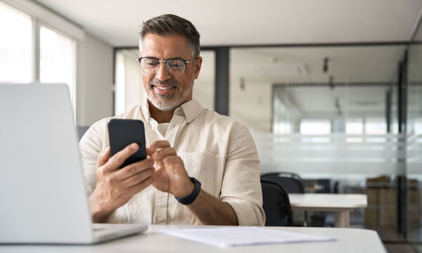 Ein Mann am Arbeitsplatz mit Smartphone und Laptop.