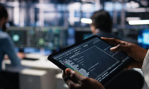 Ein Mann hält in einem Rechenzentrum ein Tablet in der Hand.